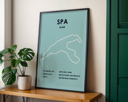 Framed poster of a race track layout on a wooden shelf with a plant.
