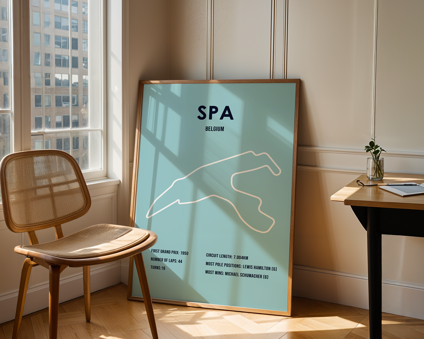 Framed poster of a race track layout with 'SPA Belgium' text in a room with a chair and table.