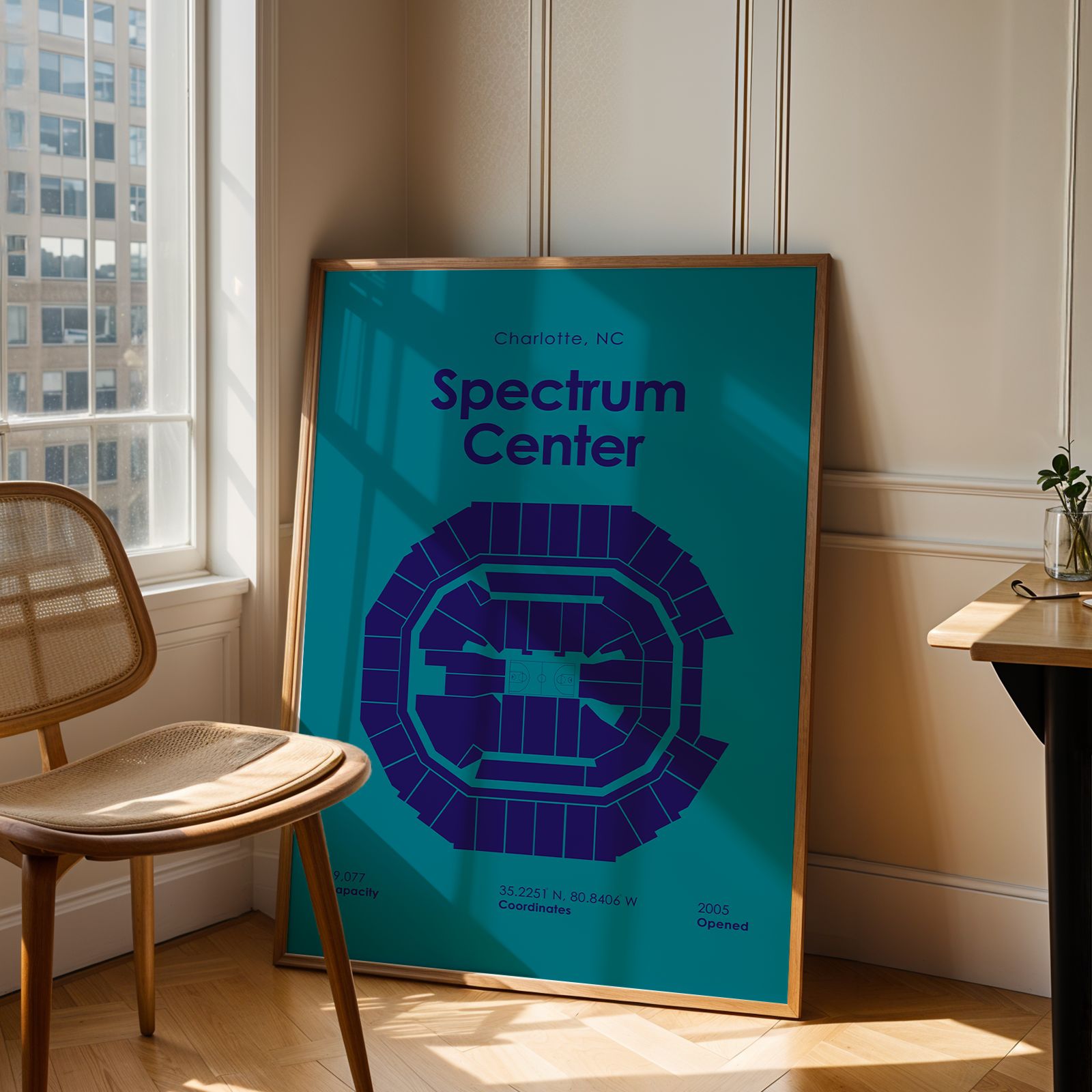 Framed poster of Spectrum Center in Charlotte, NC, leaning against a wall in a room with a chair and window.