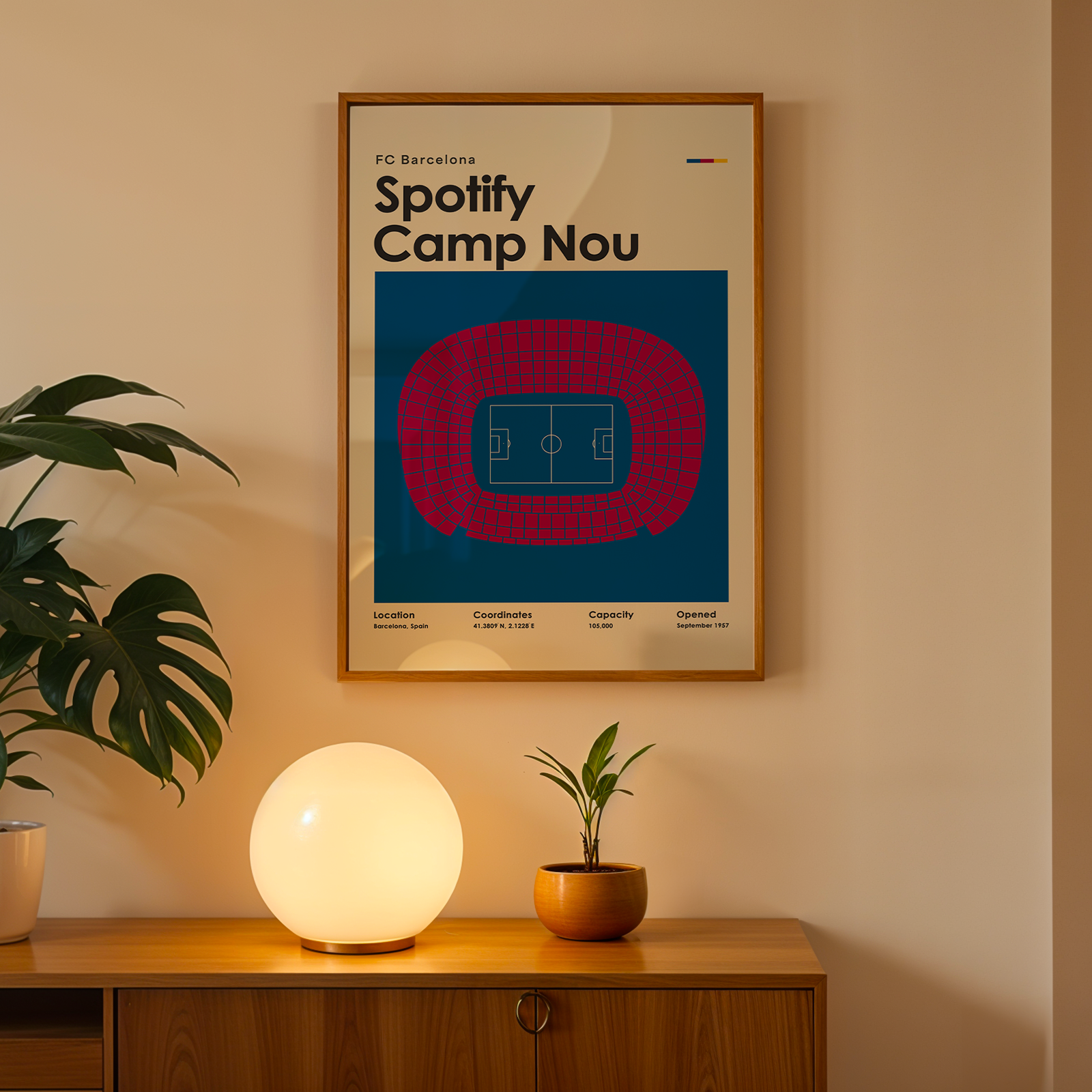 Framed poster of FC Barcelona's Spotify Camp Nou on a wall with a lamp and plant below.