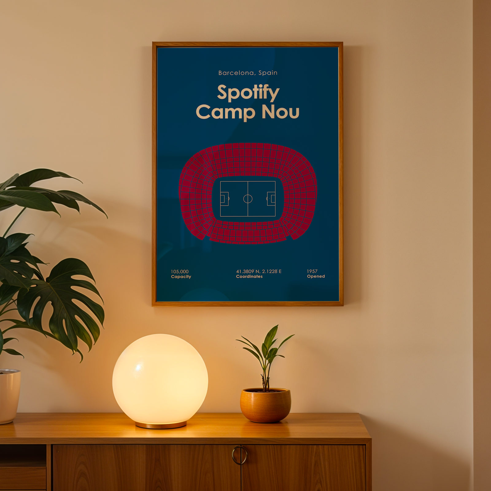 Framed poster of Spotify Camp Nou on a wall with a lamp and plant below.