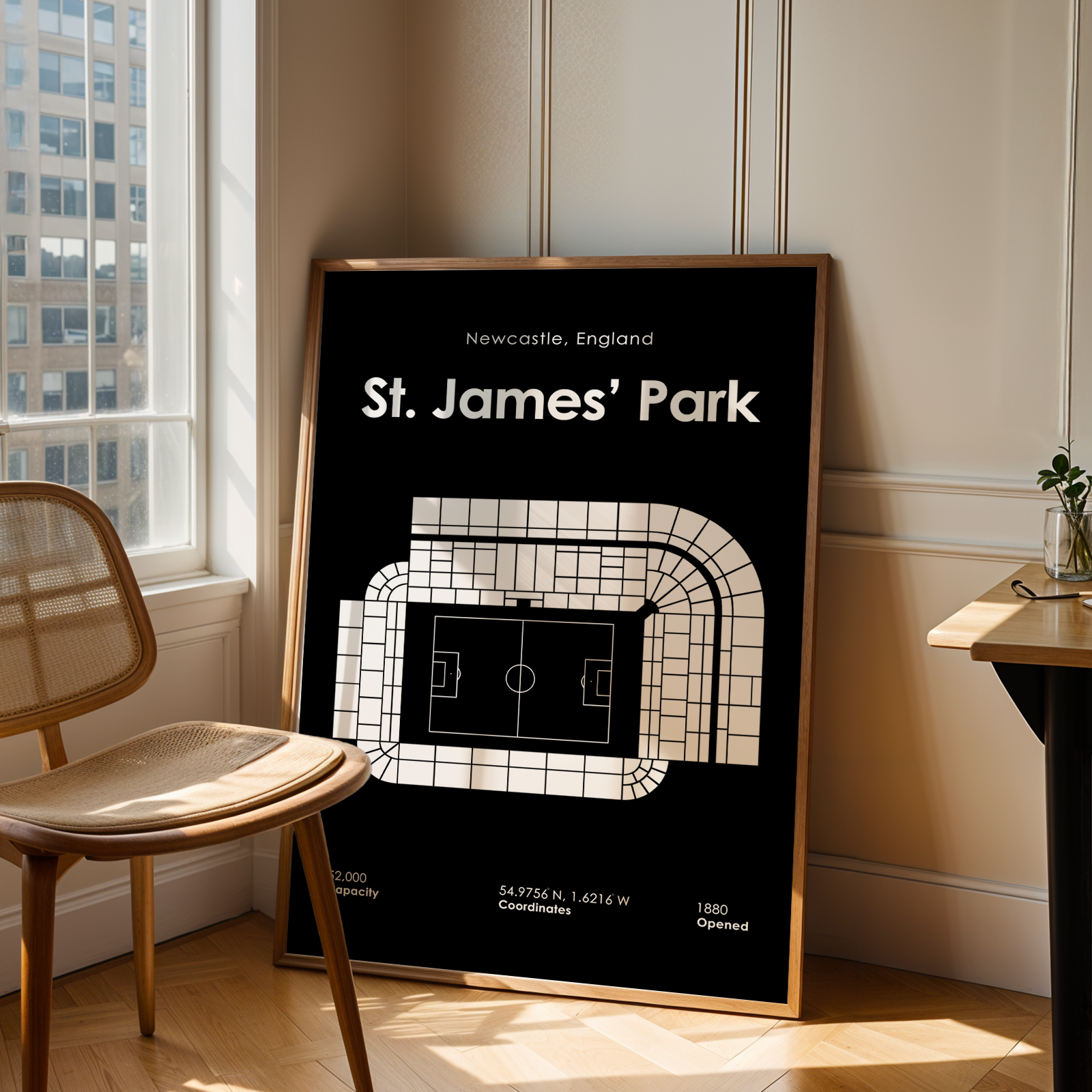 Framed poster of St. James' Park in Newcastle, England, on a wall in a room with a window and chair.