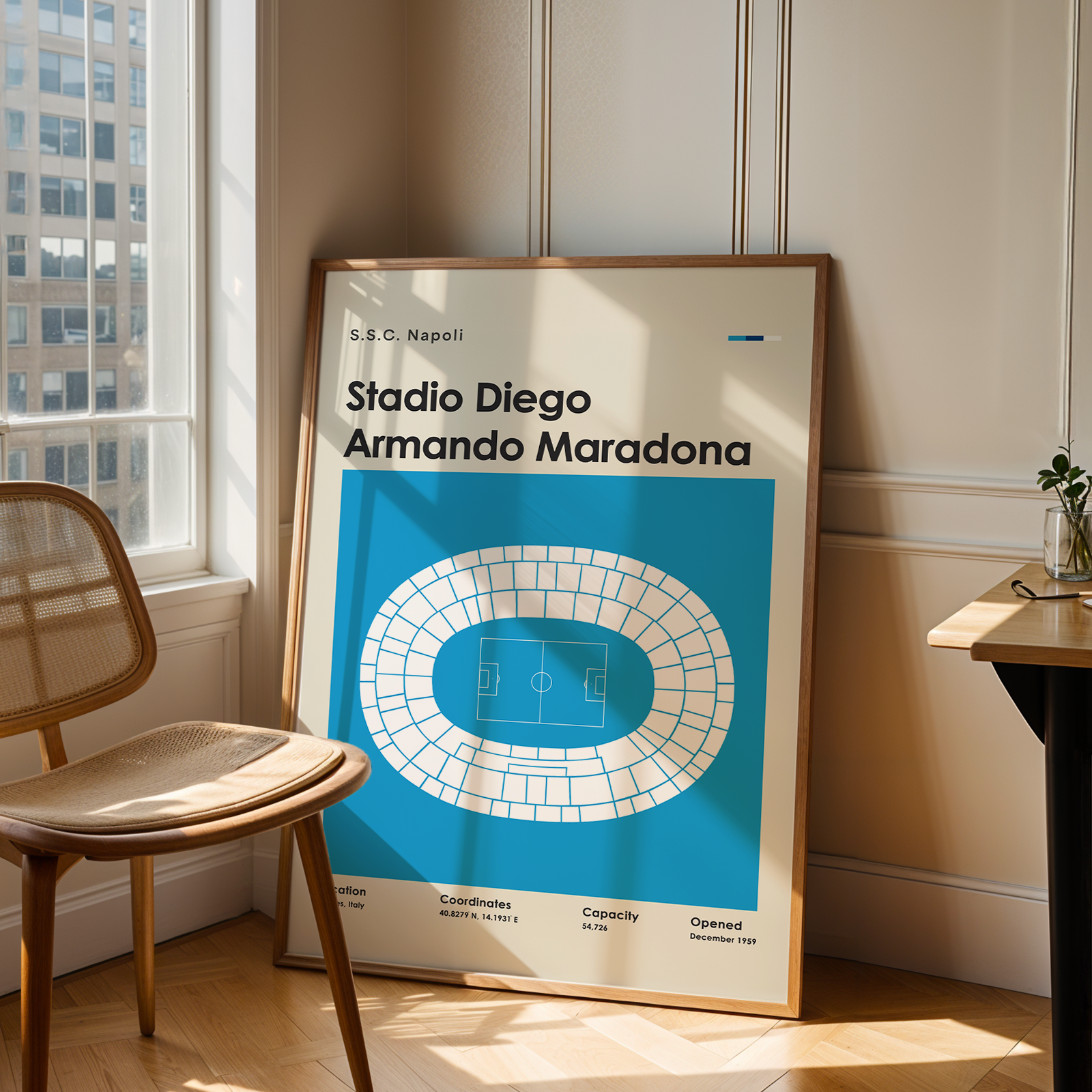 Framed poster of Stadio Diego Armando Maradona in a room with a chair and table.
