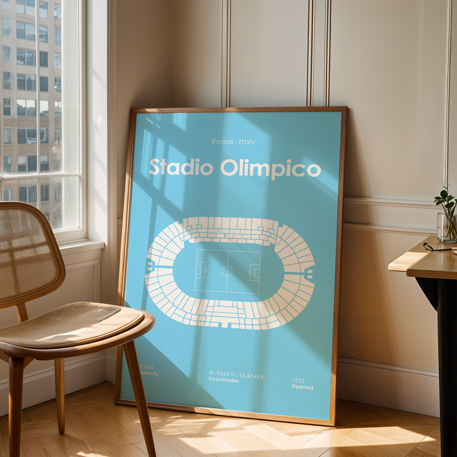 Framed poster of Stadio Olimpico in a room with a chair and window.