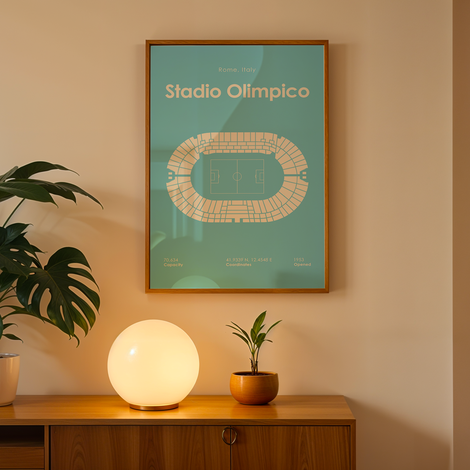 Framed poster of Stadio Olimpico on a wall with a lamp and plant below.