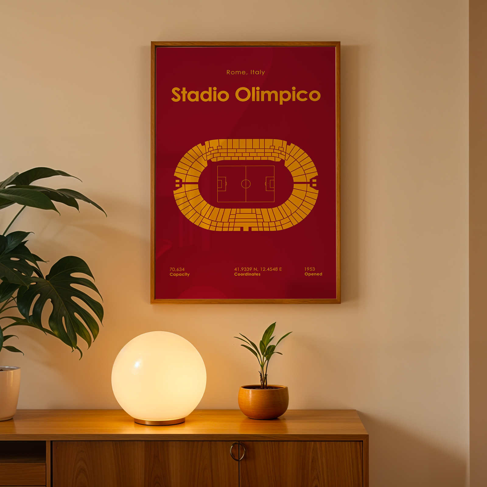 Framed poster of Stadio Olimpico on a wall with a lamp and plant below.