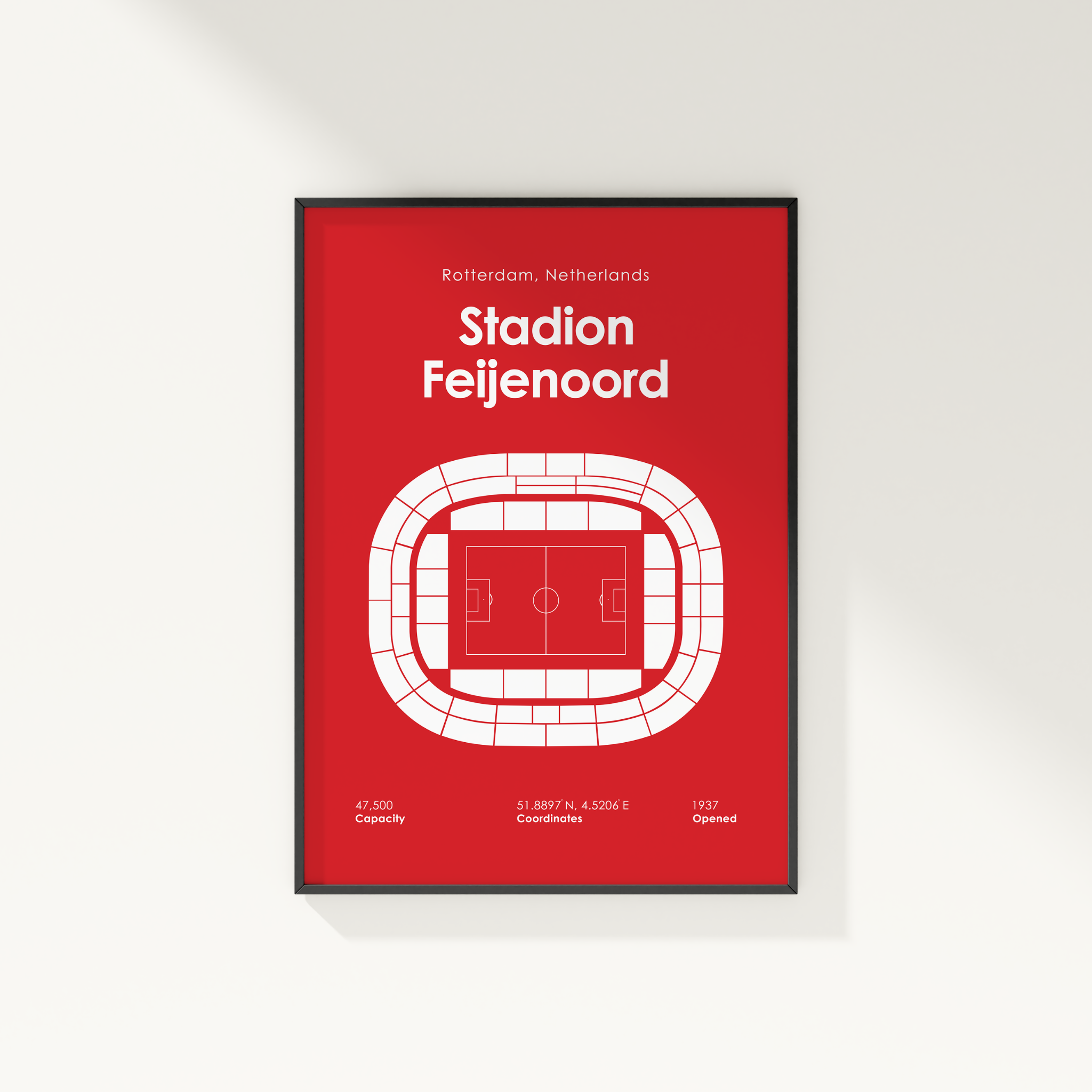 A framed red sports poster of Stadion Feijenoord in Rotterdam, Netherlands, featuring a white stadium floor plan and text details, shown hanging on a light gray wall.