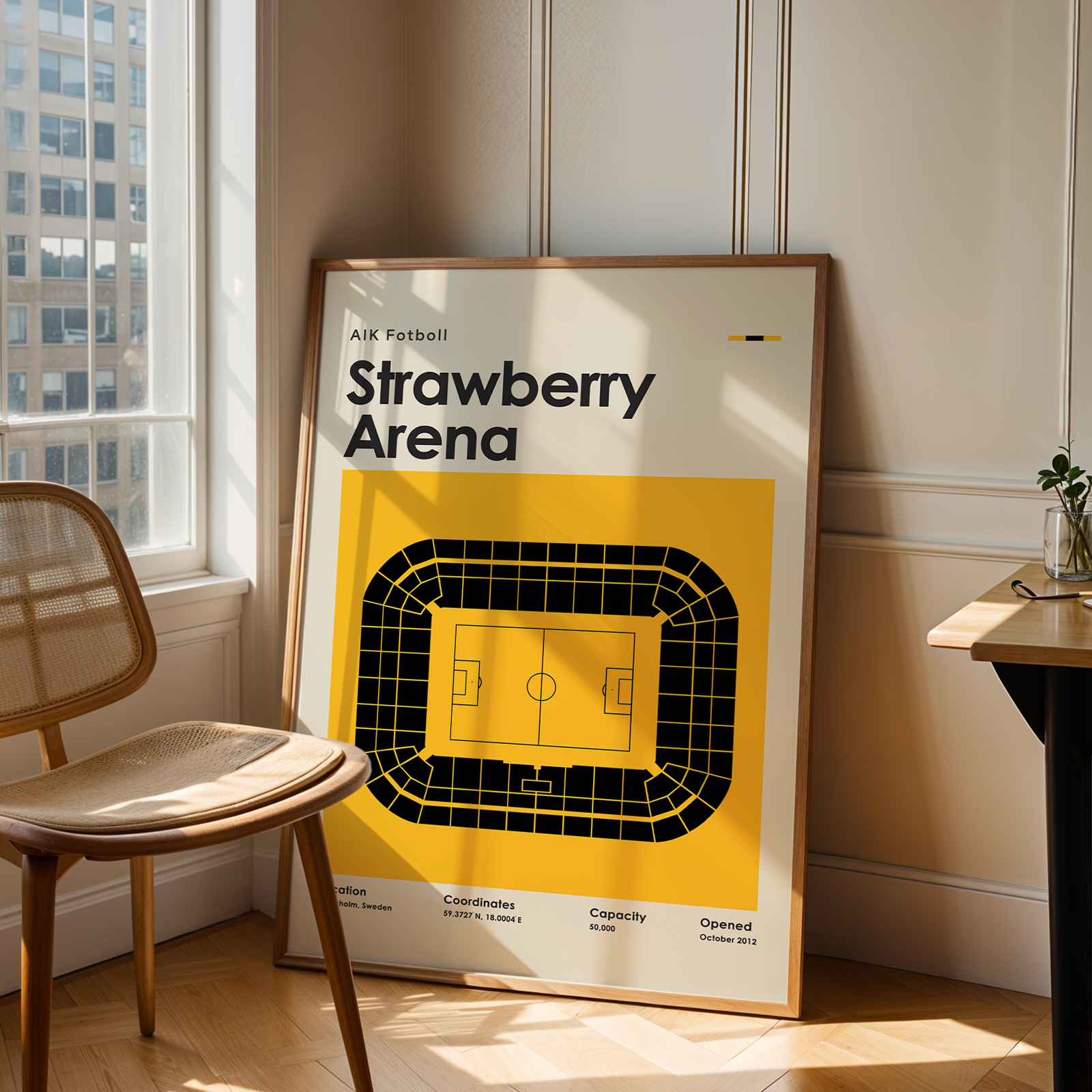 Framed poster of Strawberry Arena in a room with a window and chair.