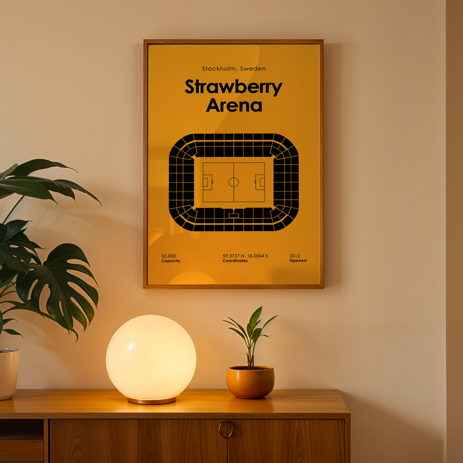 Framed poster of Strawberry Arena on a wall with a plant and lamp below.