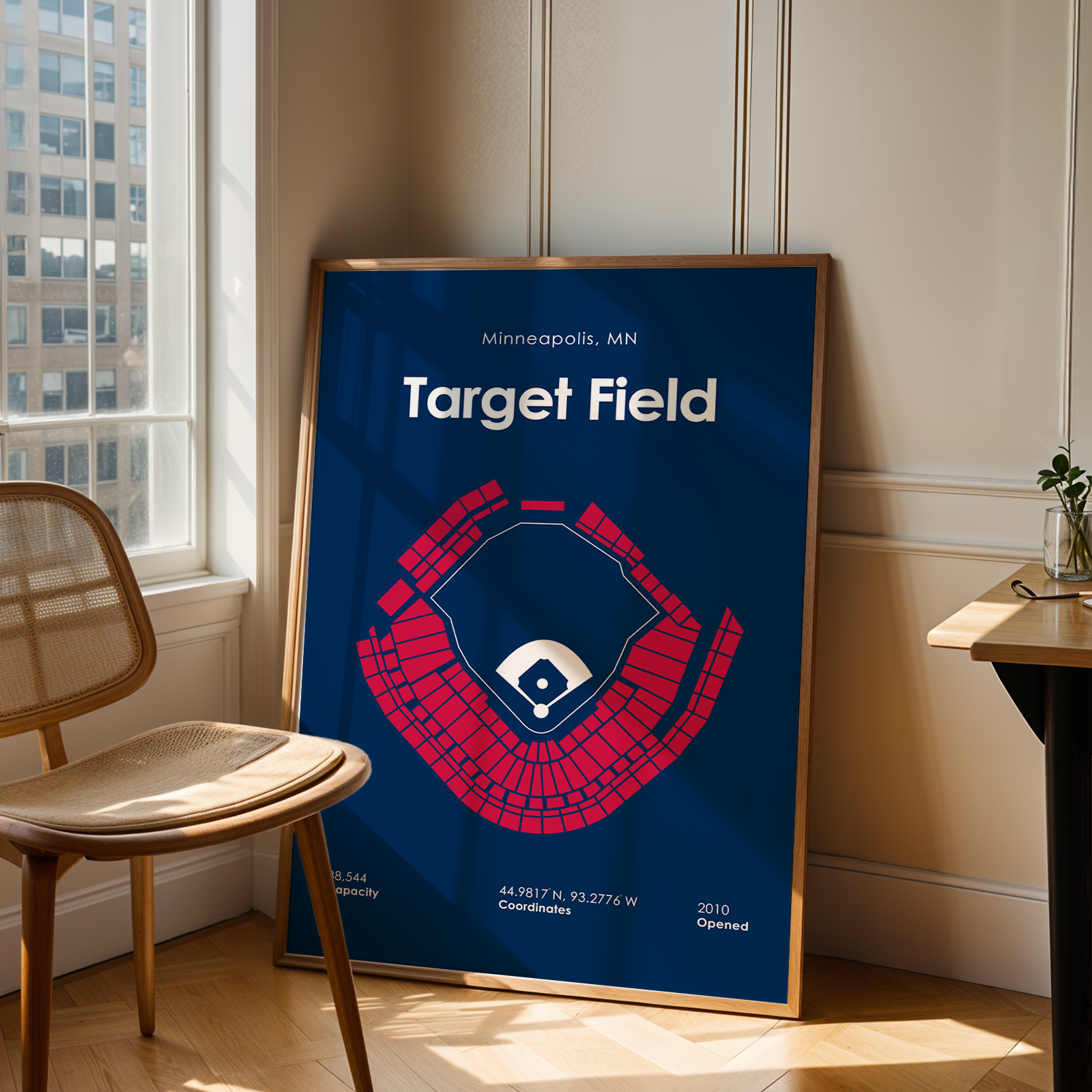 Framed poster of Target Field in Minneapolis, MN, leaning against a wall in a room with a window and chair.
