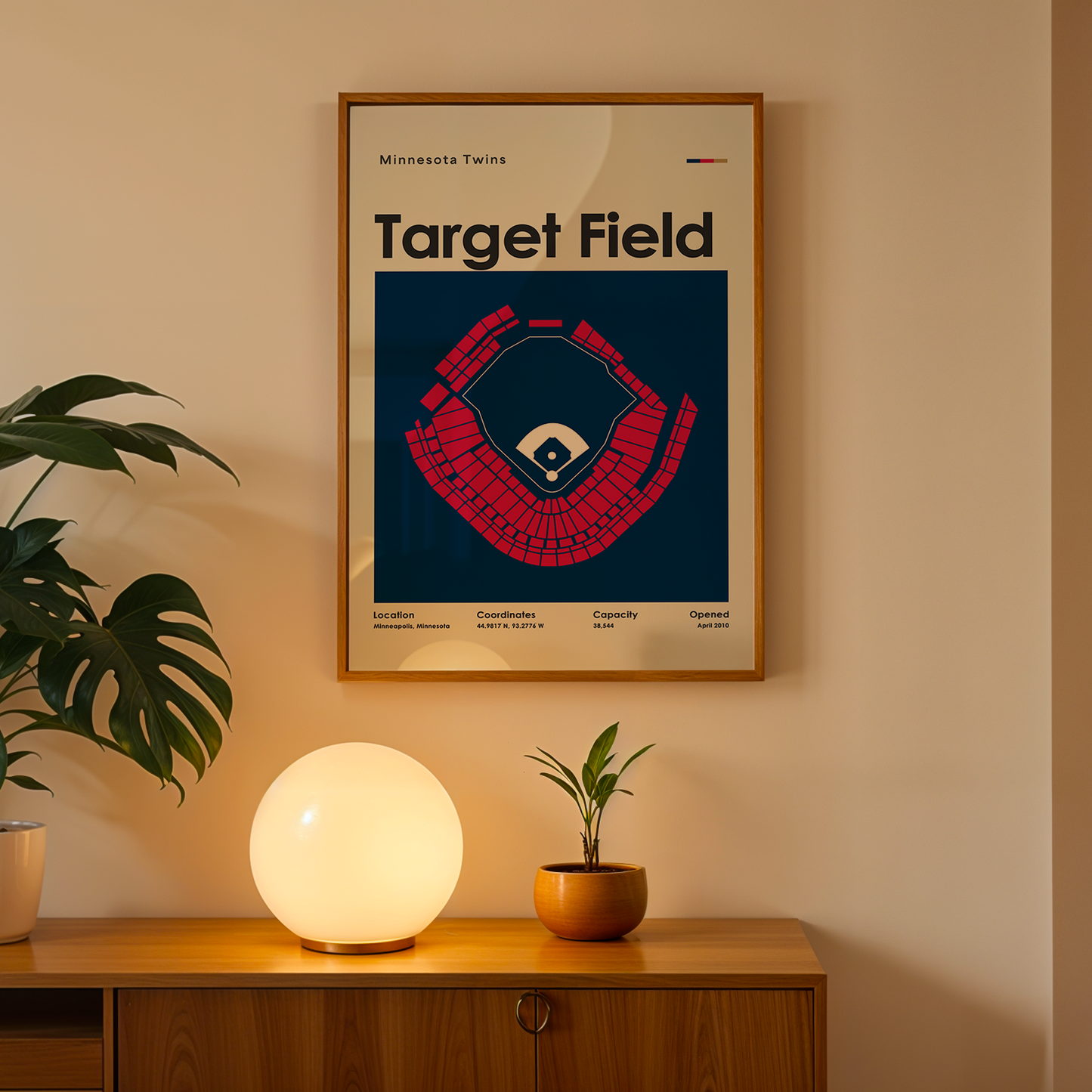 Framed poster of Target Field on a wall above a wooden cabinet with decorative items.