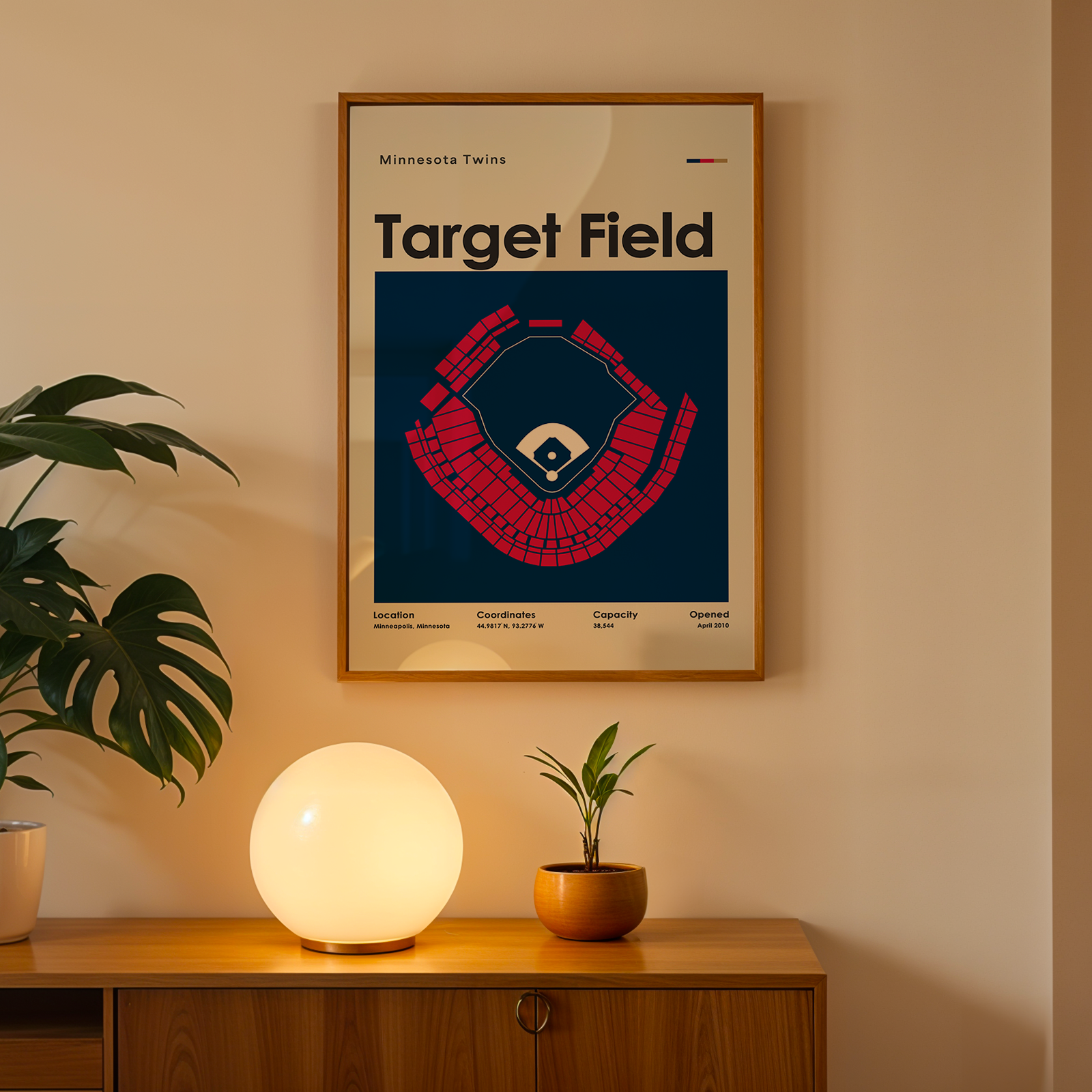 Framed poster of Target Field on a wall above a wooden cabinet with decorative items.