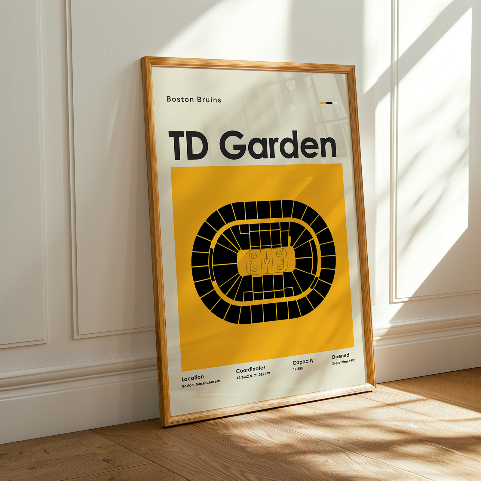 Framed poster of TD Garden with 'Boston Bruins' text on a yellow background, leaning against a white wall.