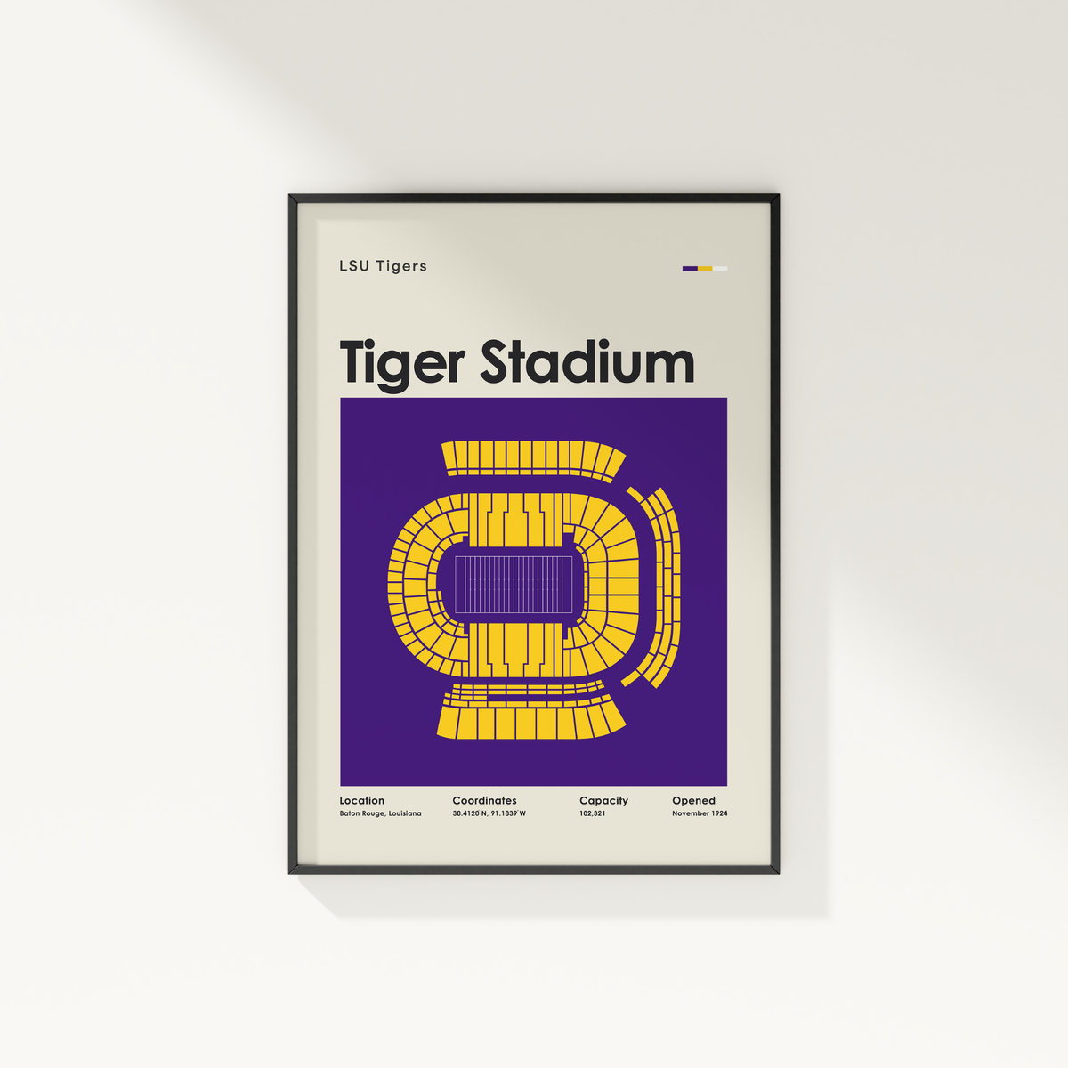A framed LSU Tigers Tiger Stadium poster hanging on a white wall. The poster features a purple background with a yellow stadium layout and black text, enclosed in a thin black frame.