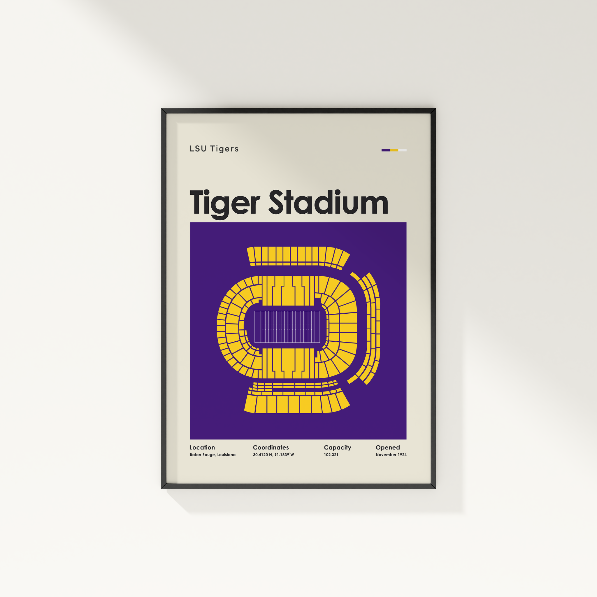 A framed LSU Tigers Tiger Stadium poster hanging on a white wall. The poster features a purple background with a yellow stadium layout and black text, enclosed in a thin black frame.
