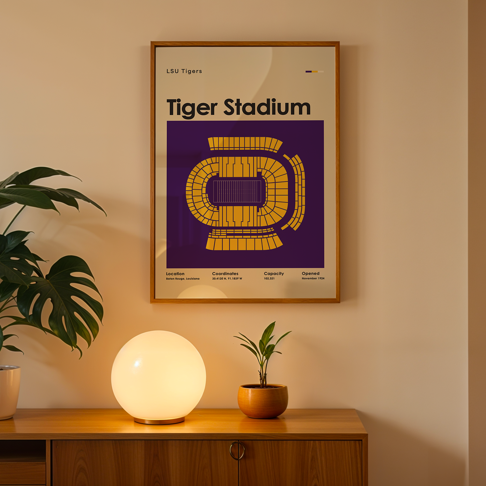 A framed poster of the LSU Tigers Tiger Stadium design hangs on a beige wall above a wooden console table. The poster features a purple background with a yellow stadium graphic and the text 'LSU Tigers Tiger Stadium'.