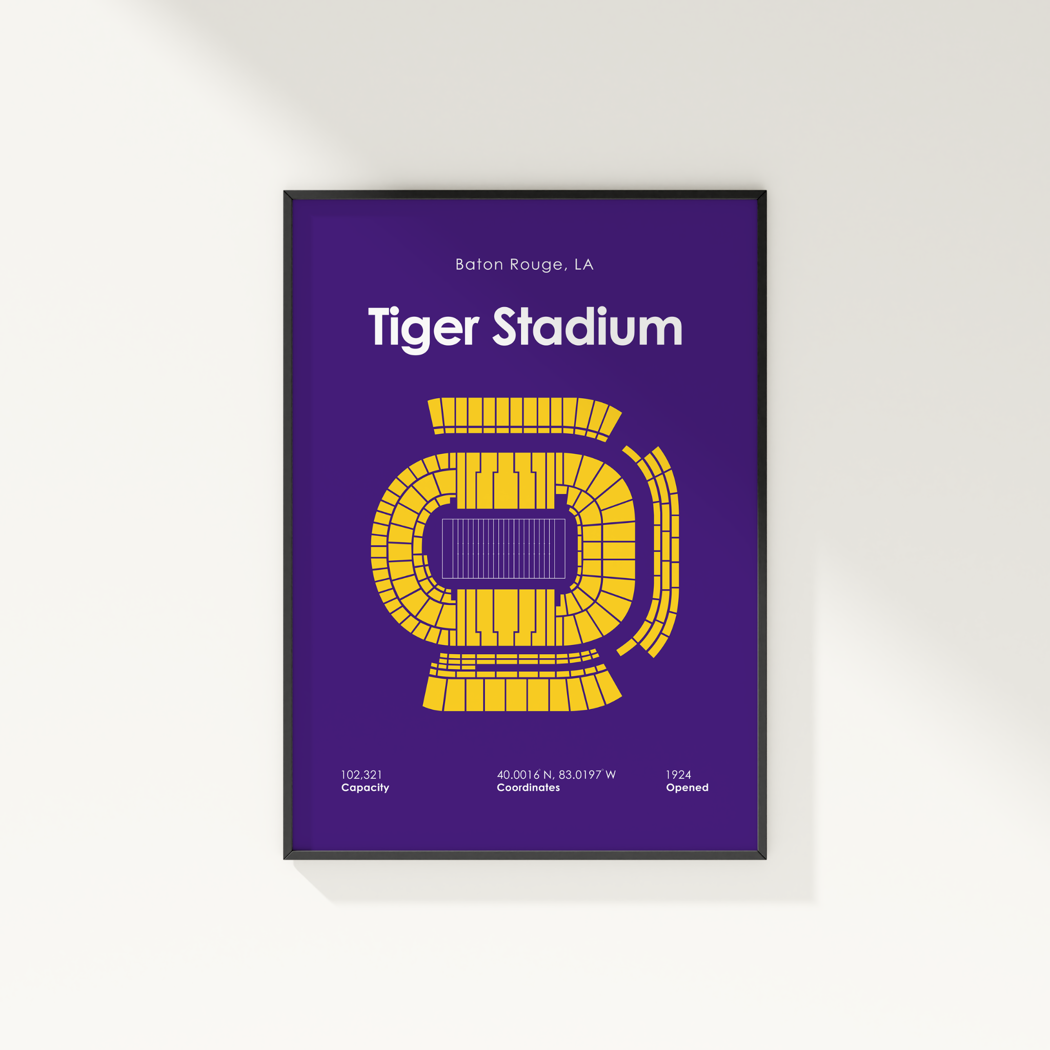 A framed vertical poster of Tiger Stadium in Baton Rouge, LA, featuring a purple background with a yellow stadium layout and white text, shown hanging on a white wall.