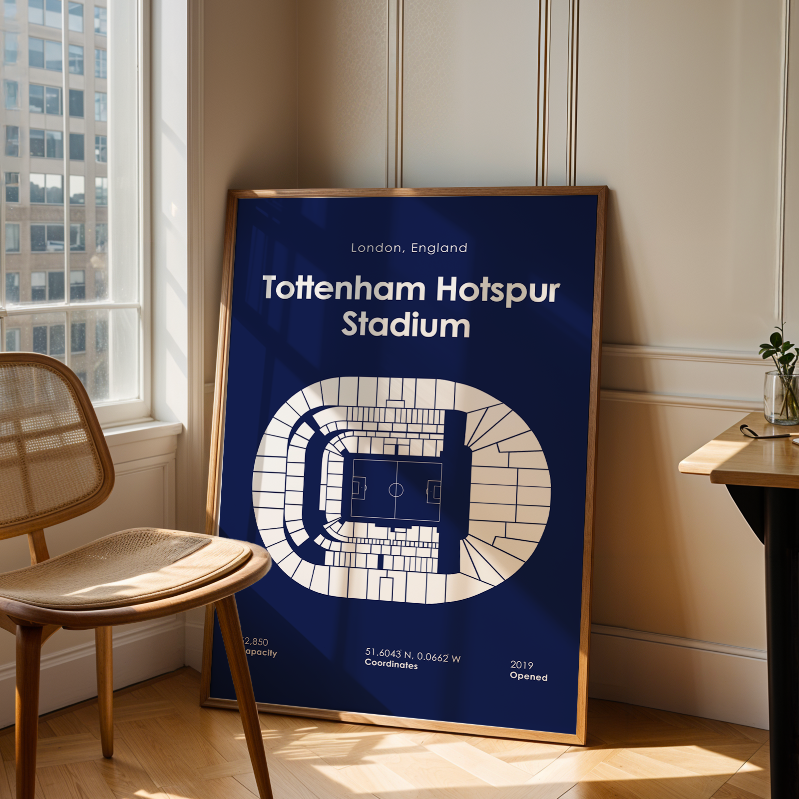 Framed poster of Tottenham Hotspur Stadium layout in a room with a window and chair.