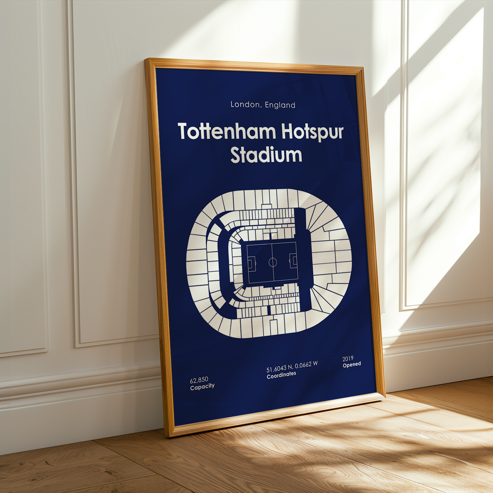 Framed poster of Tottenham Hotspur Stadium layout on a blue background, leaning against a white wall.
