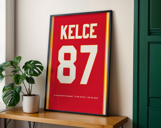 Framed sports jersey with 'KELCE 87' on a wooden shelf with a plant.
