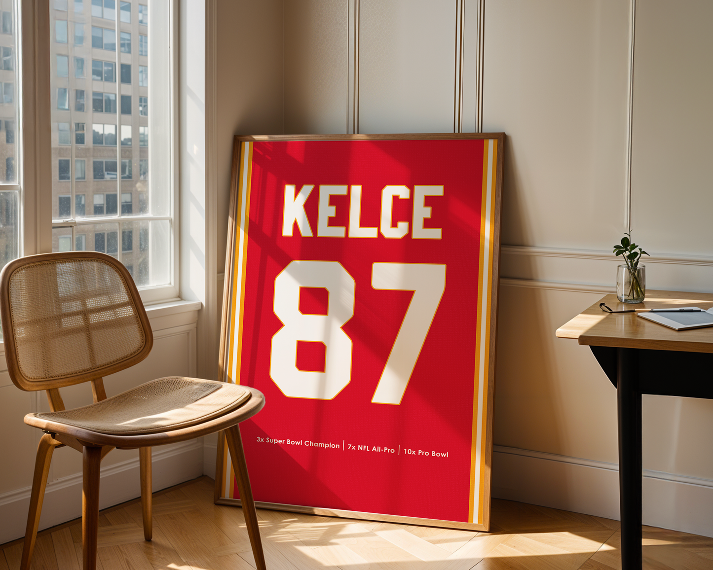 Framed sports jersey with 'KELCE 87' on a wall in a room with a chair and table.