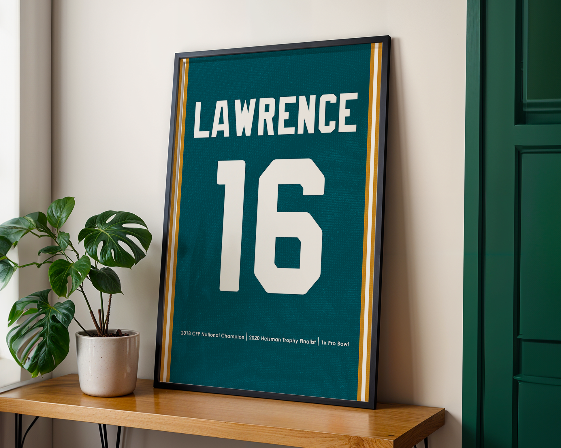 Framed poster with 'Lawrence 16' on a wooden shelf with a plant.