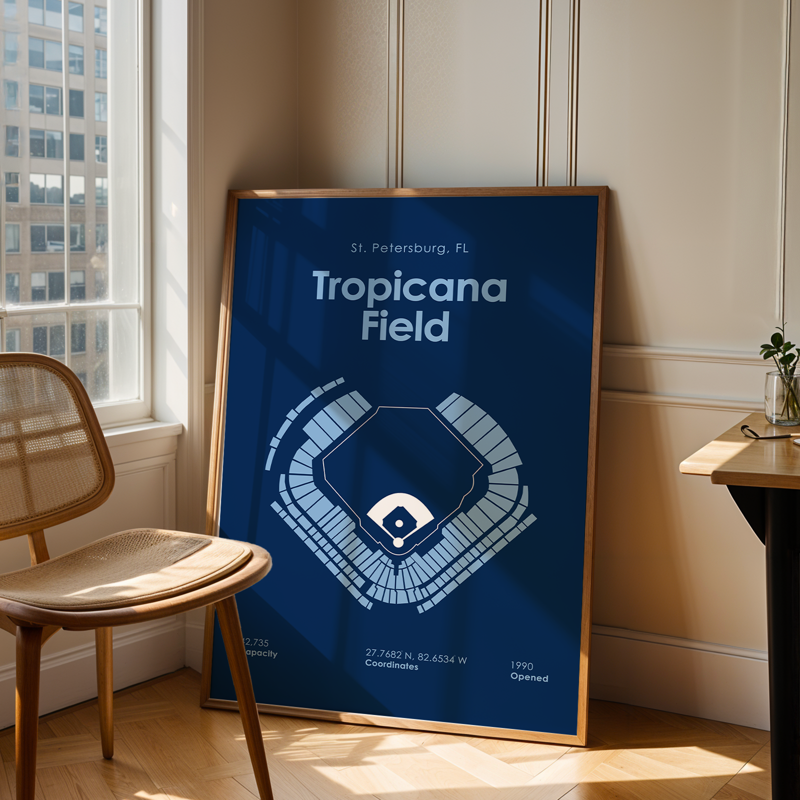 Framed poster of Tropicana Field in a room with a window and chair.