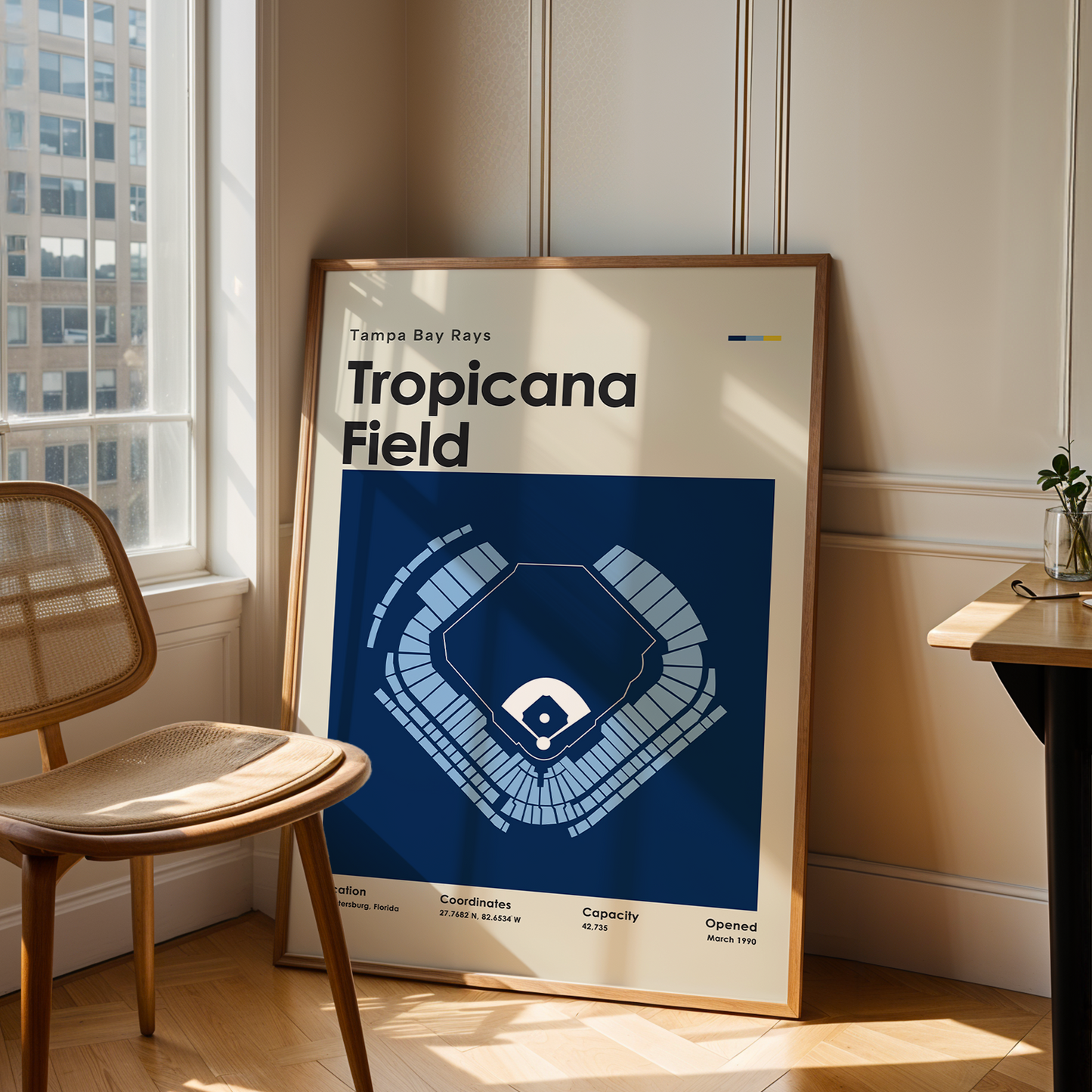 Framed poster of Tropicana Field in a room with a chair and table.