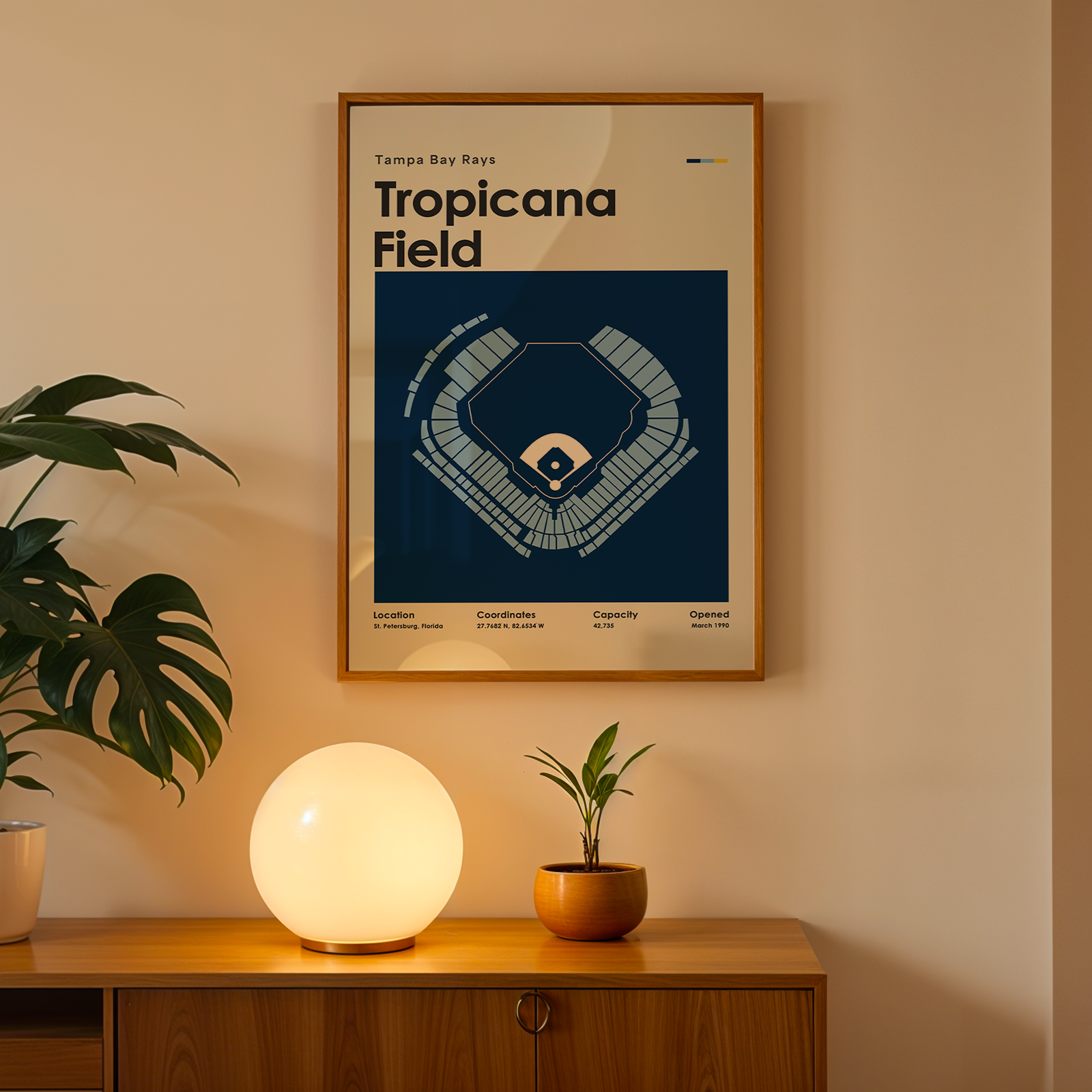 Framed Tropicana Field poster on a wall above a wooden cabinet with decorative items.