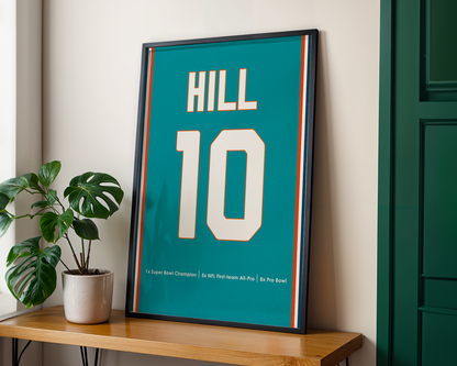 Framed sports jersey with 'HILL 10' on a wooden shelf next to a plant