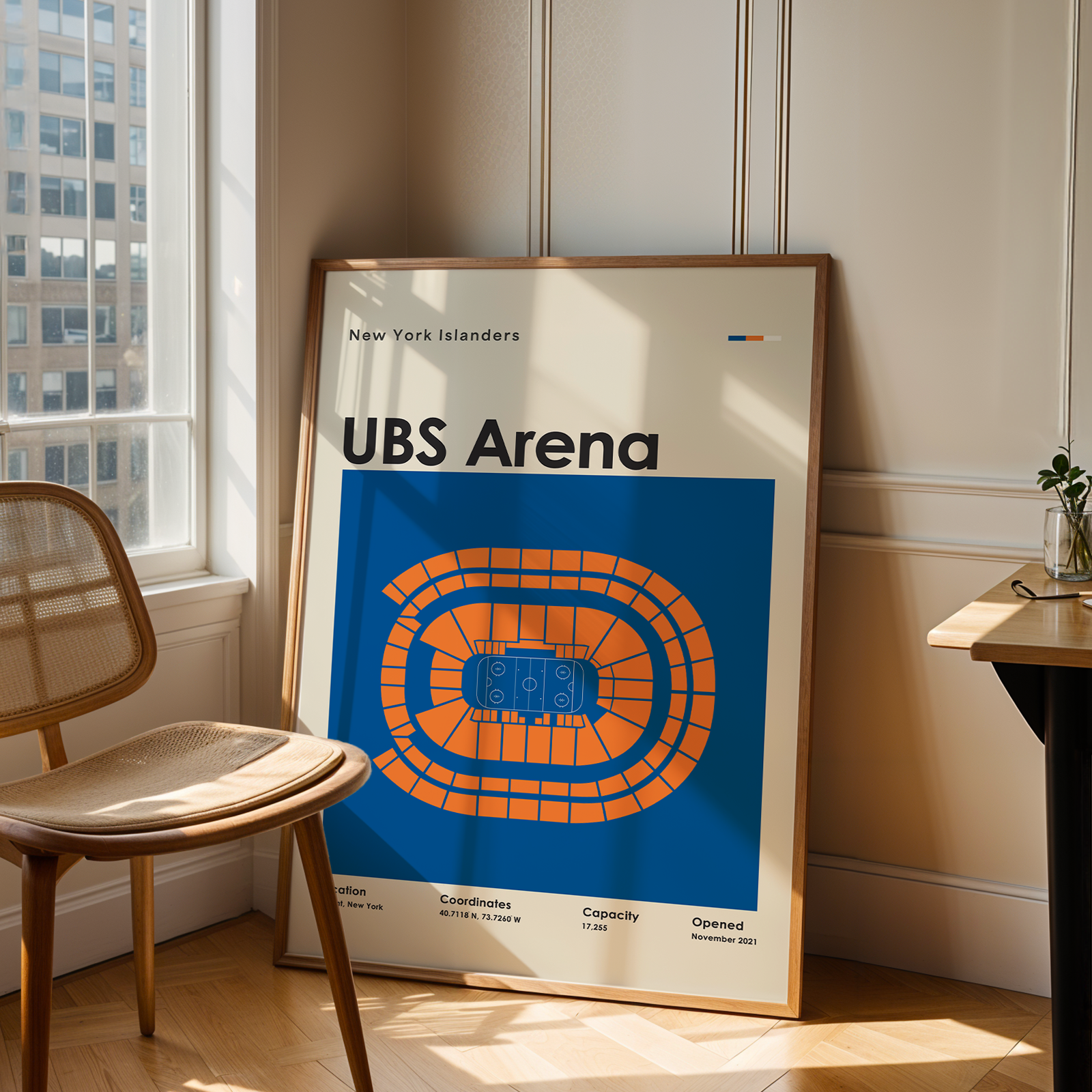 Framed poster of UBS Arena in a room with a chair and table.