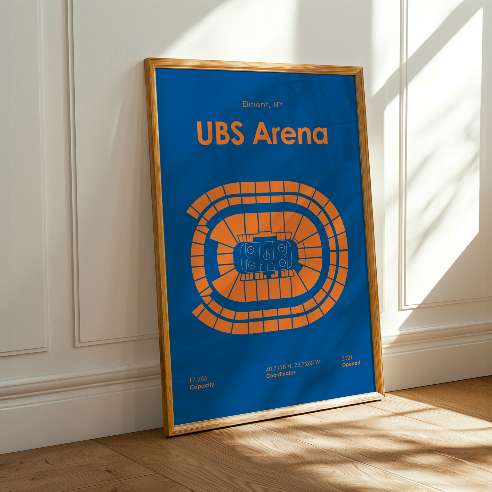 Framed poster of UBS Arena with blue background and orange text and design, leaning against a white wall.