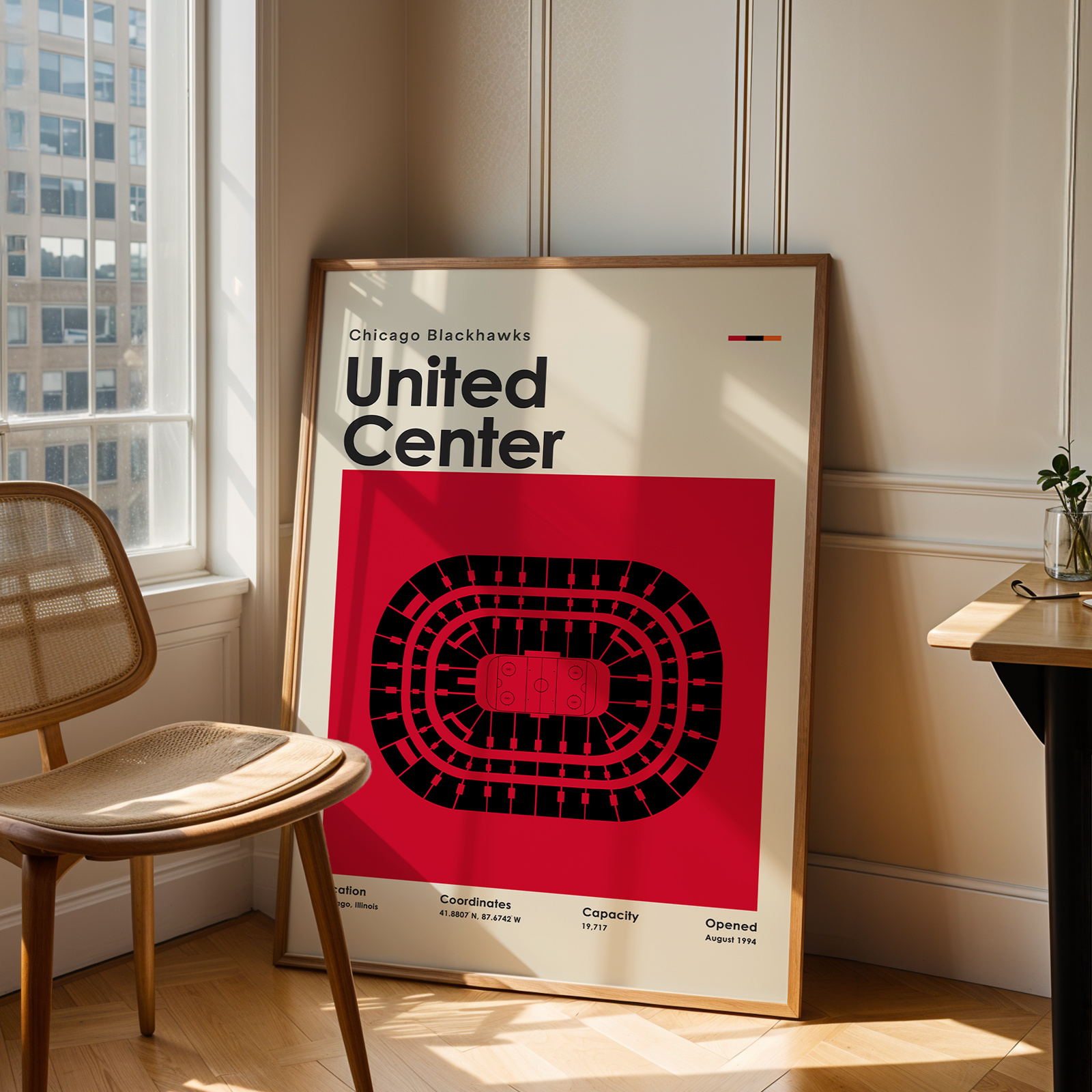 Framed poster of the United Center in Chicago Blackhawks design leaning against a wall in a room with a chair and table.