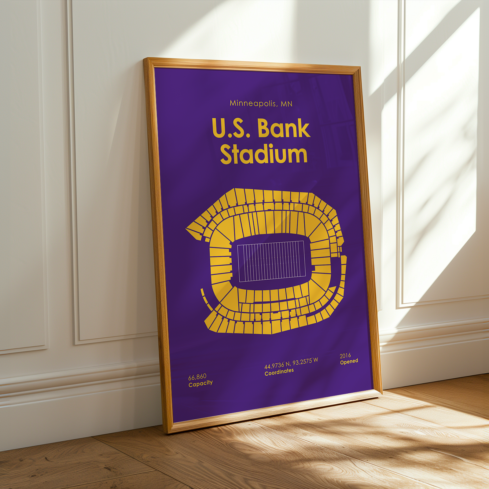 Framed poster of U.S. Bank Stadium with purple background and yellow seating chart, leaning against a white wall.