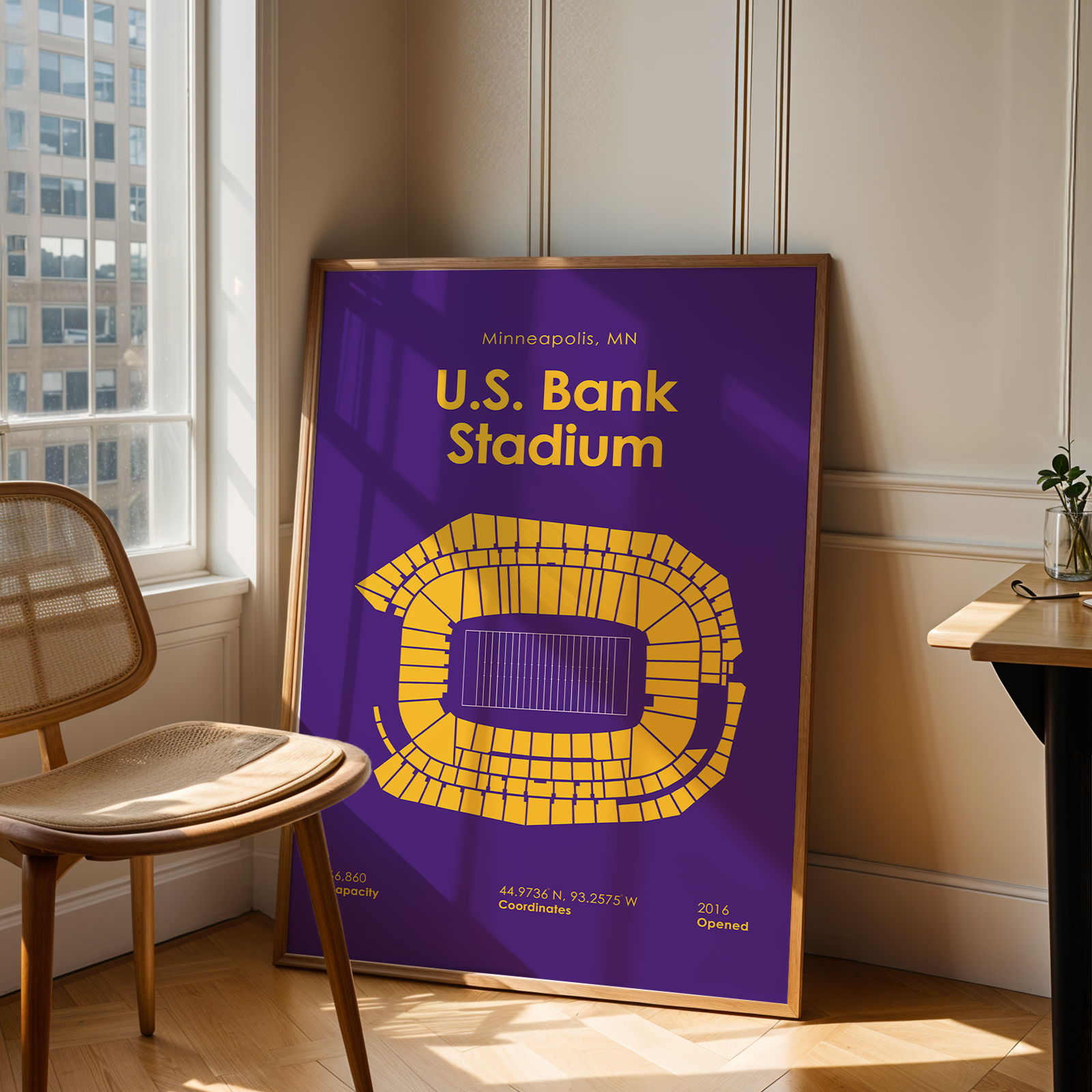 Framed poster of U.S. Bank Stadium in a room with a chair and table.