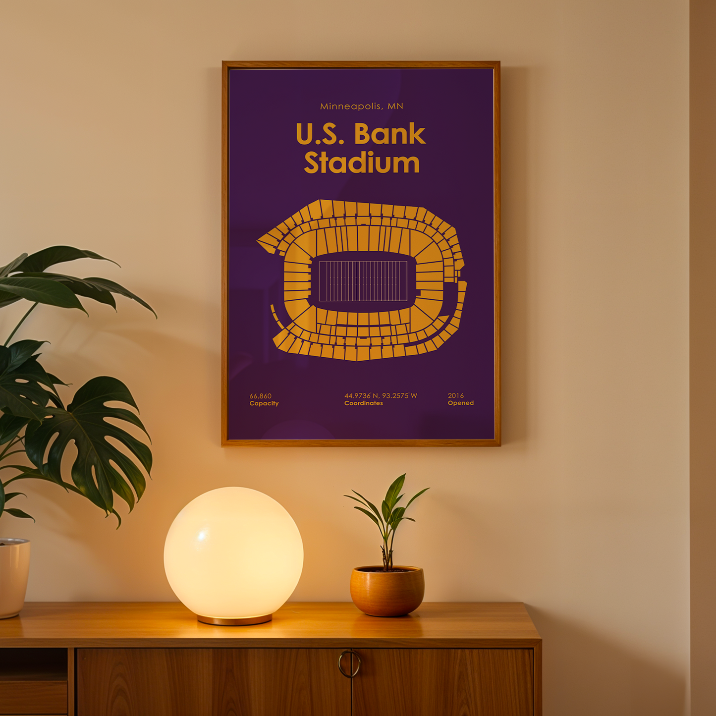 Framed poster of U.S. Bank Stadium on a wall above a wooden cabinet with decorative items.