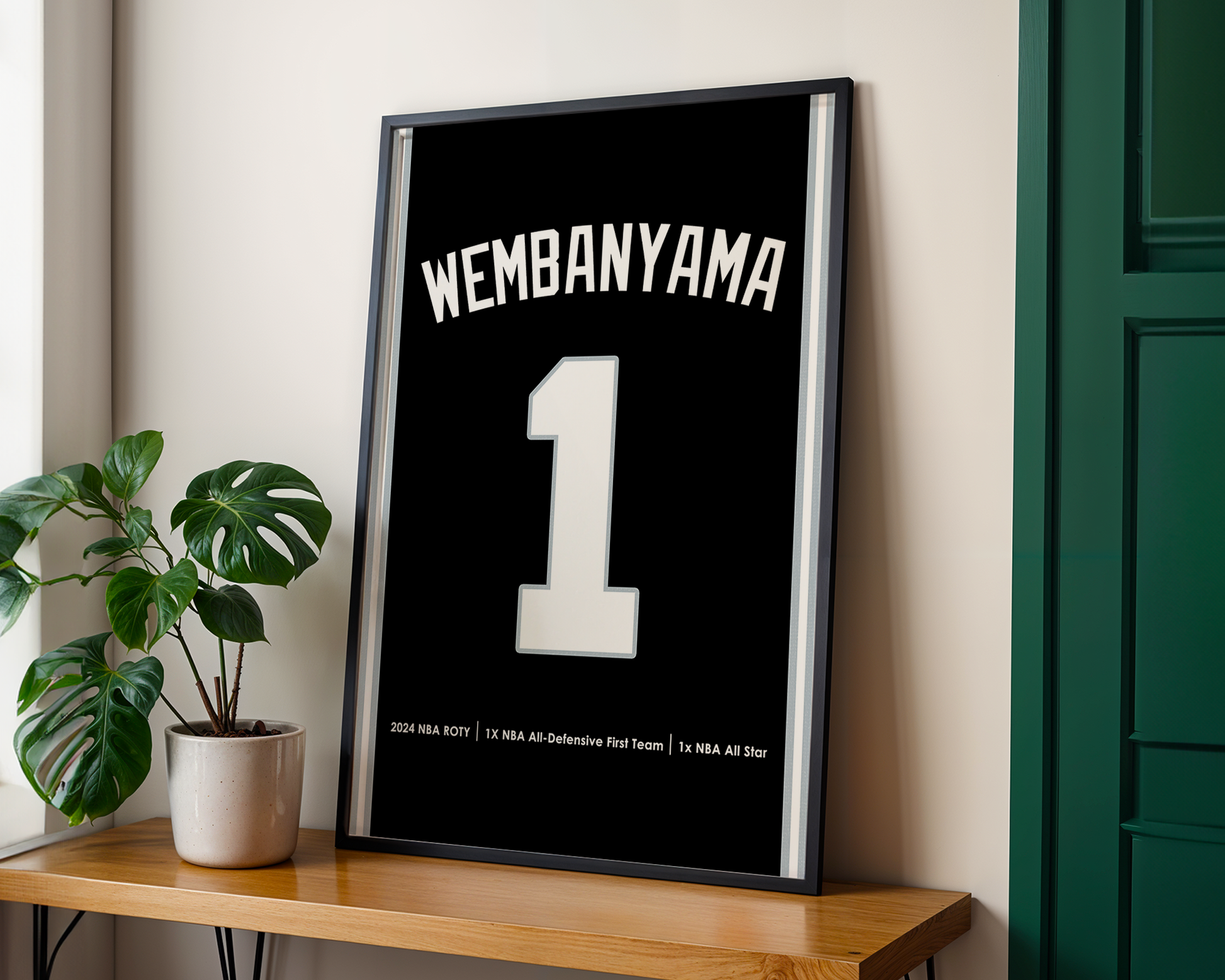 Framed poster with 'Wembanyama 1' on a wooden table with a plant in the background
