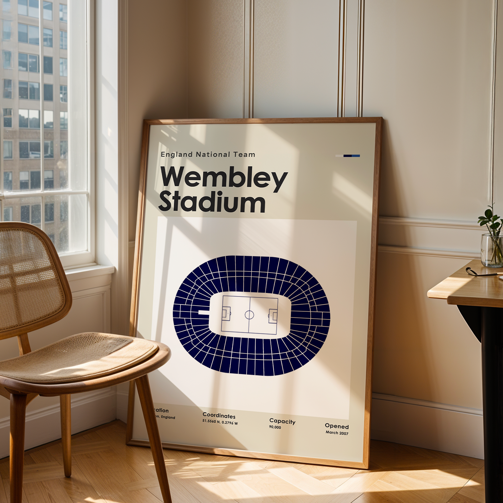 Framed poster of Wembley Stadium in a room with a chair and table.