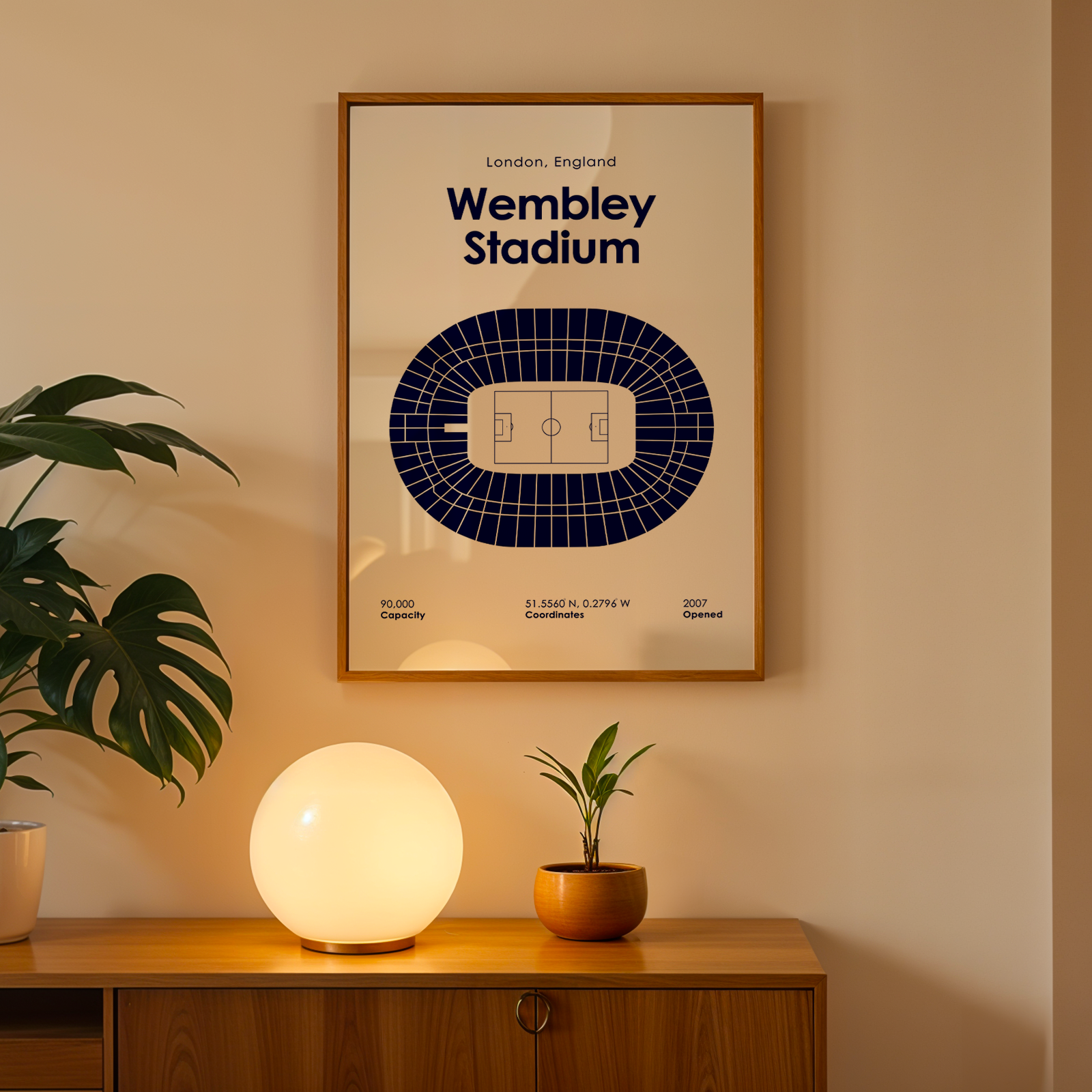 Framed Wembley Stadium map on a wall with a lamp and plant below.