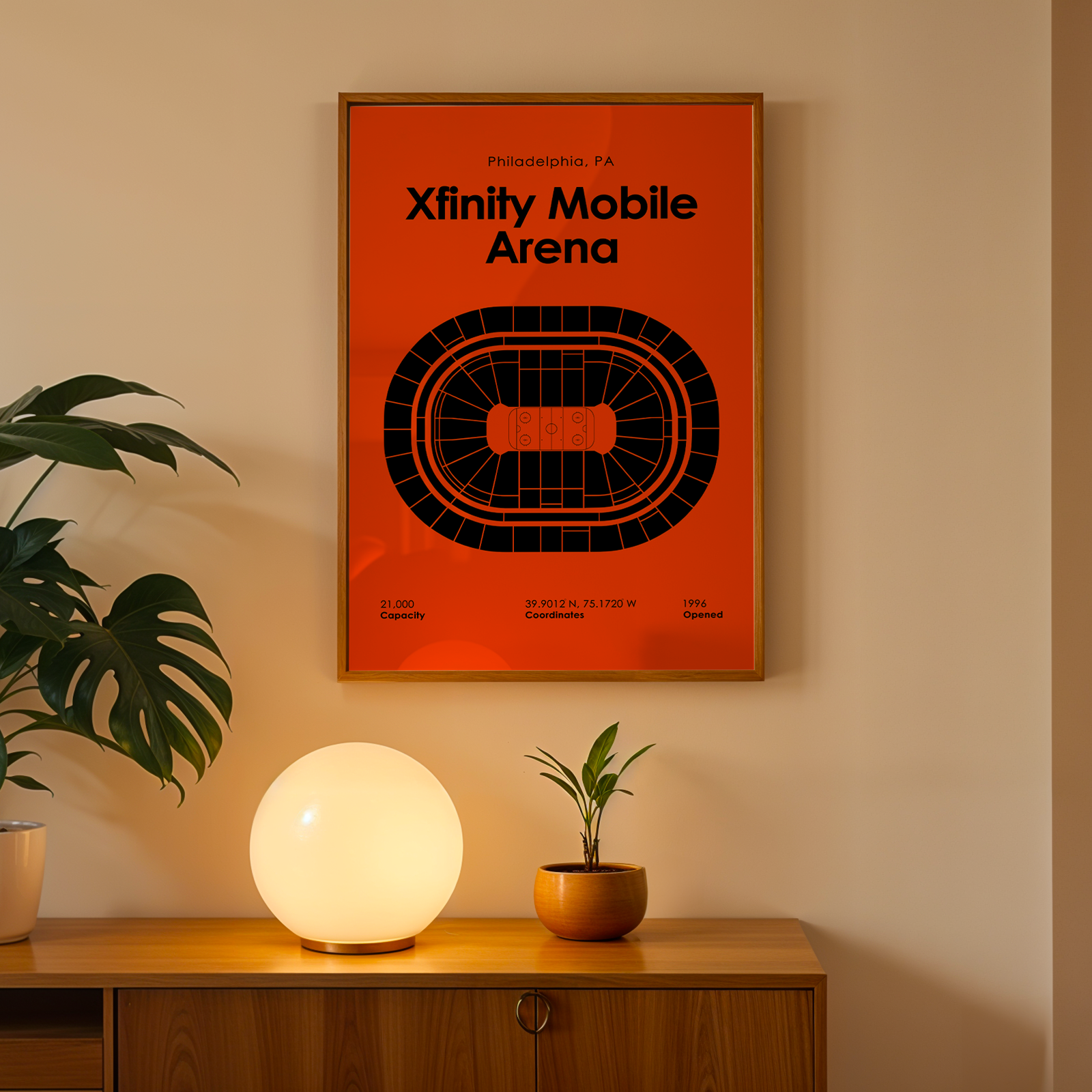 Framed poster of Xfinity Mobile Arena on a wall with a plant and lamp below.
