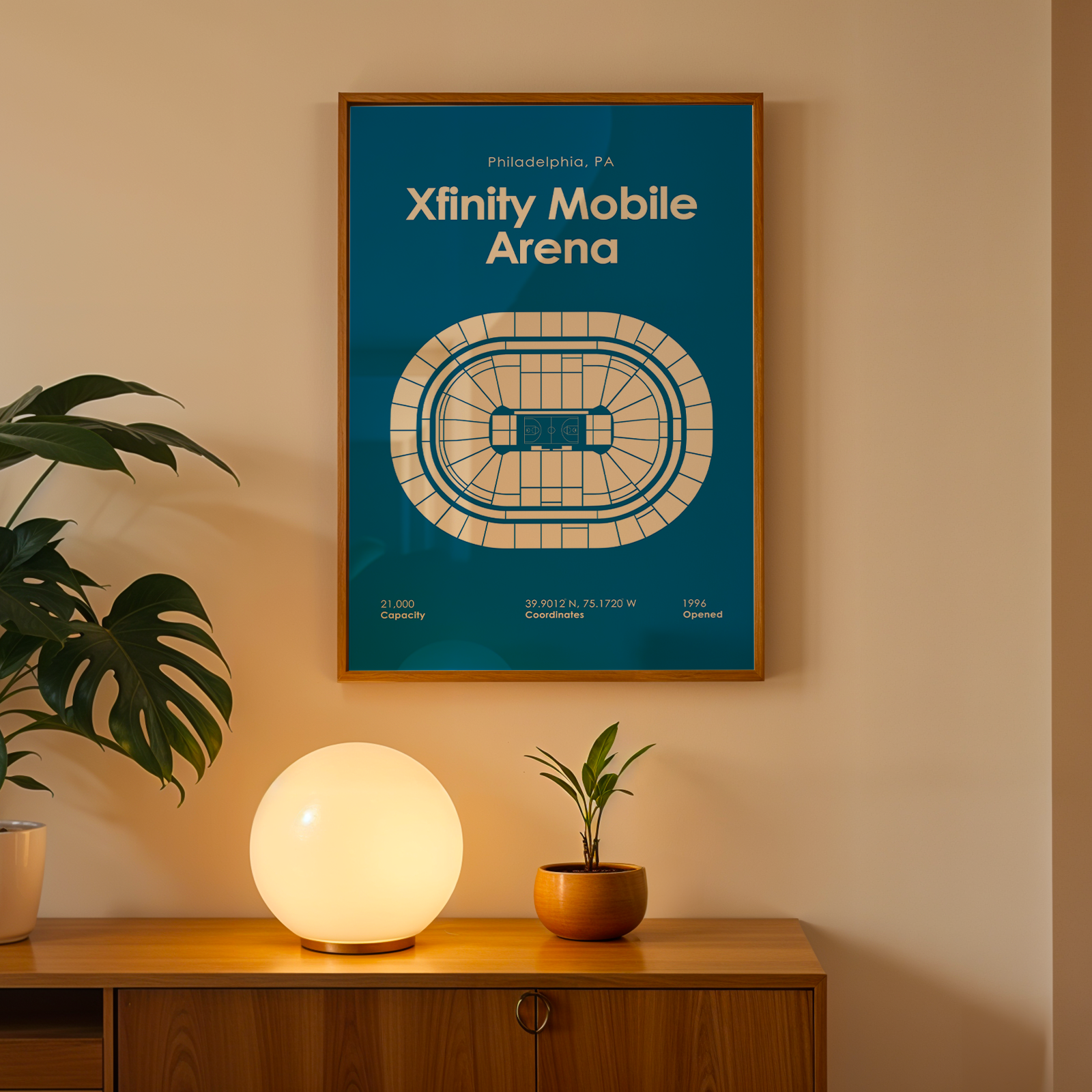 Framed poster of Xfinity Mobile Arena on a wall above a wooden cabinet with decorative items.