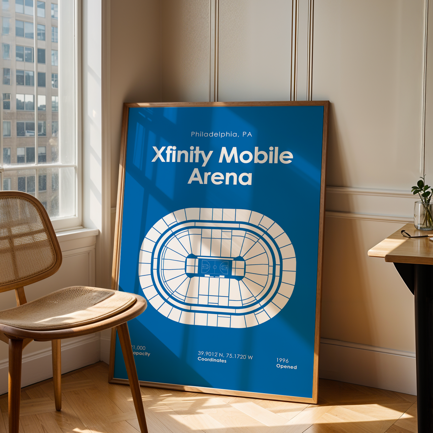 Framed poster of Xfinity Mobile Arena in Philadelphia, PA, leaning against a wall in a room with a chair and window.
