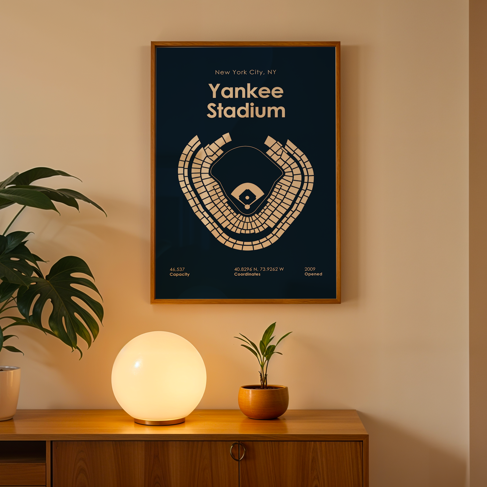 Framed poster of Yankee Stadium on a wall with a plant and lamp below.